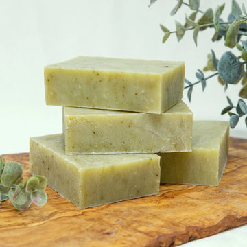 Poofy Organics Eucalyptus Spearmint soap bars stacked on wood with eucalyptus leaves
