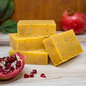 Poofy Organics Pomegranate Pear soap bars stacked beside a cut pomegranate