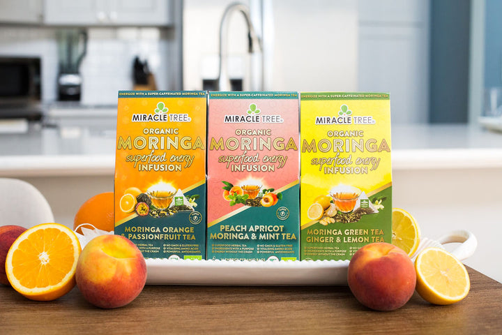 Orange Passionfruit, Peach Mint Apricot and Ginger Lemon moringa energy tea boxes with fresh fruit.