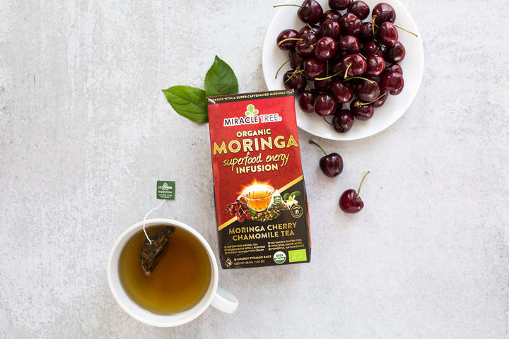 Cherry Chamomile moringa energy tea box with fresh cherries and a cup of tea.