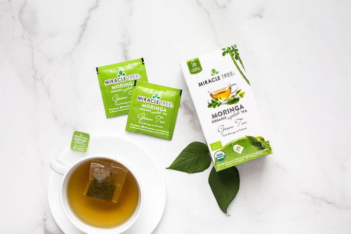 Green Tea moringa tea box and sachets beside a cup of tea.