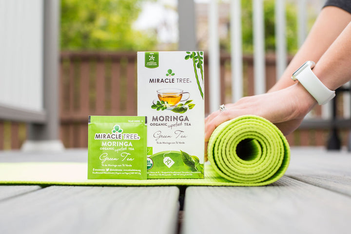 Green Tea moringa tea box and sachet outdoors next to a rolled yoga mat.