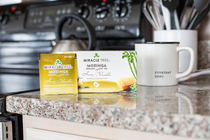 Honey & Vanilla moringa tea box and sachet on a kitchen counter beside a mug.
