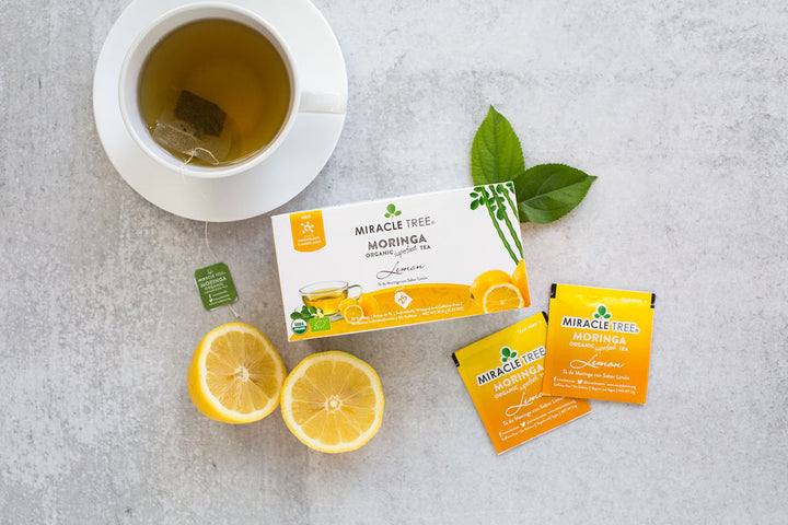 Lemon moringa tea box with sachets, lemon halves and a cup of tea.