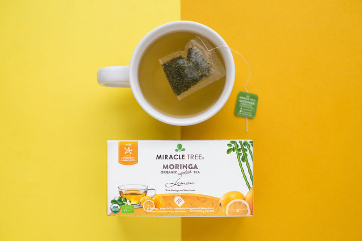 Lemon moringa tea box below a mug of tea on a yellow background.