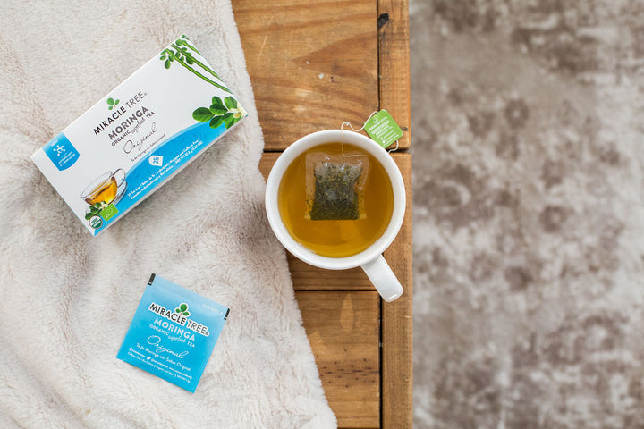Original moringa tea box and a mug of tea on a soft blanket.