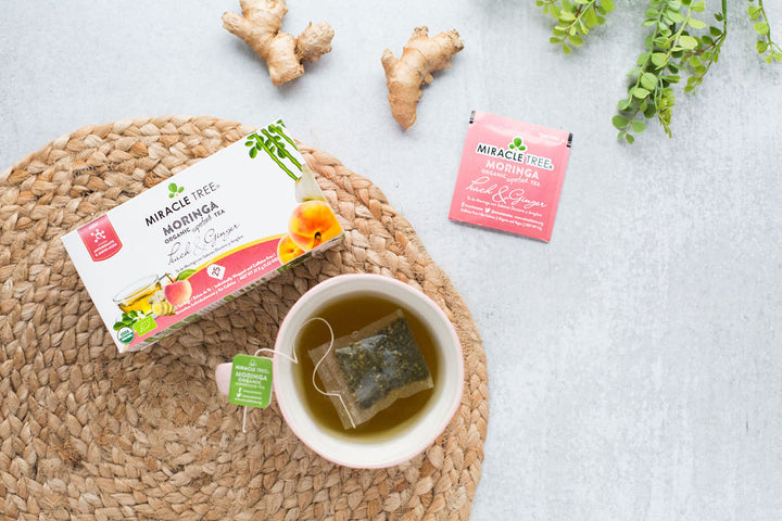 Peach & Ginger moringa tea box beside a cup of tea.