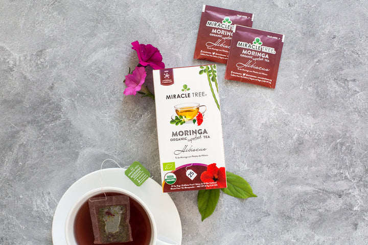 Hibiscus moringa tea box with sachets, pink flowers and a cup of tea.
