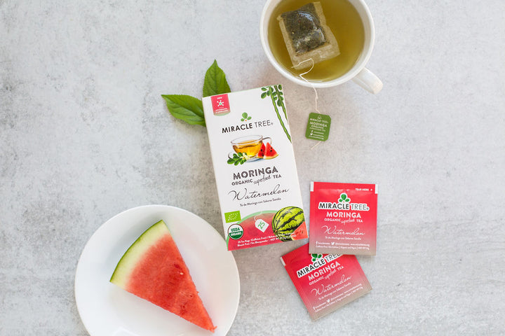 Watermelon moringa tea box with sachets, a watermelon slice and a cup of tea.